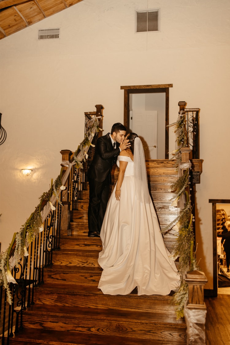 Groom kisses his bride passionately on a wooden staircase lined with greenery at one of the best wedding venues in Central Florida