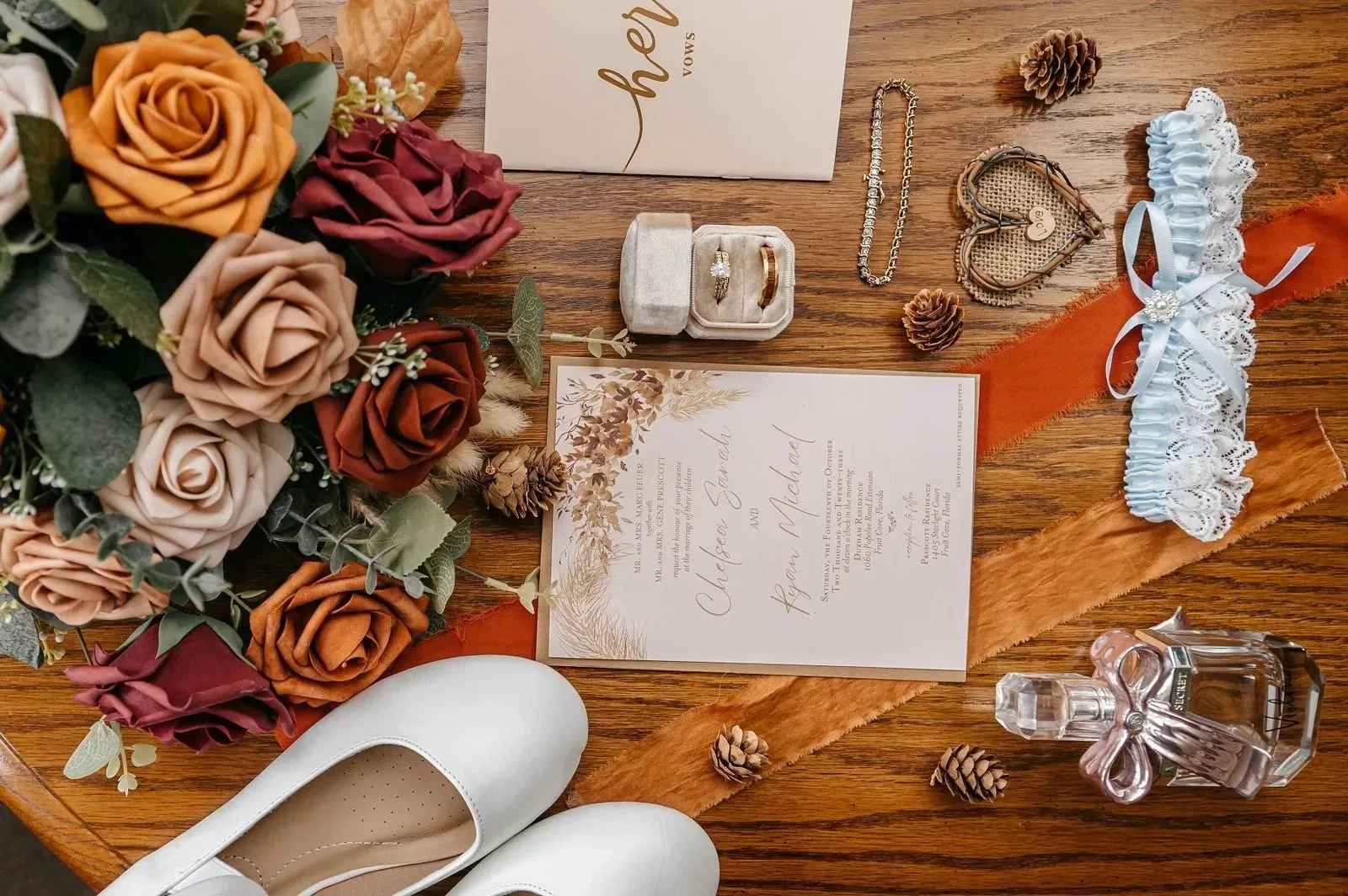A beautiful flat lay of rustic wedding details on a wooden table, featuring an invitation, rings in a velvet box, and a bouquet of orange and red roses, beautifully captured by a wedding photographer in florida.