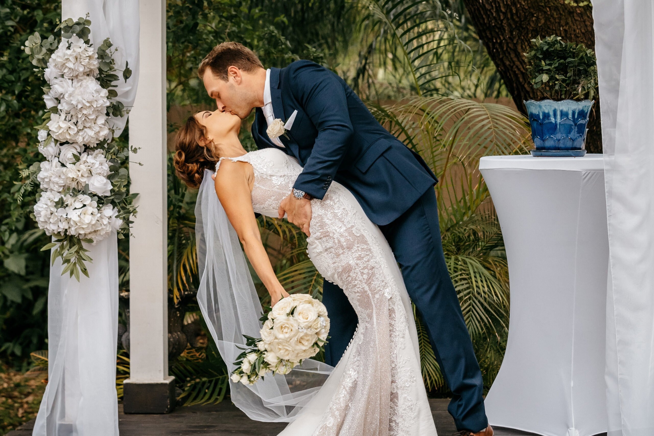 Bride and groom sharing a kiss beneath a floral wedding arch during their Florida ceremony.