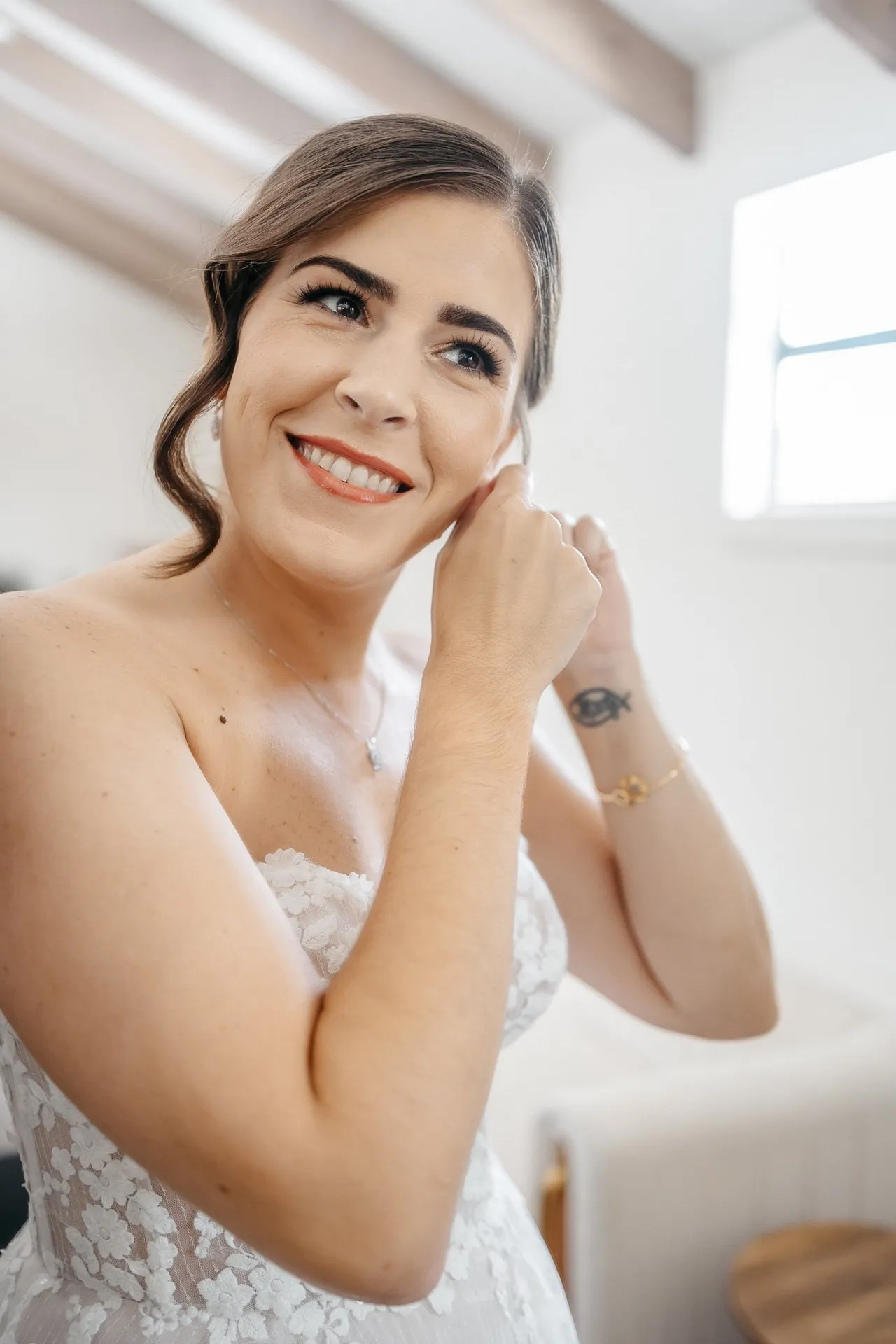 A bride smiles while putting on her earrings as she prepares to get married