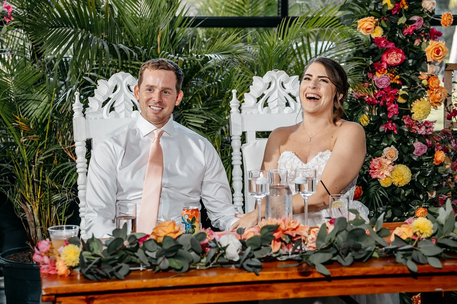 Bride and groom laugh while sitting at a table at their wedding reception