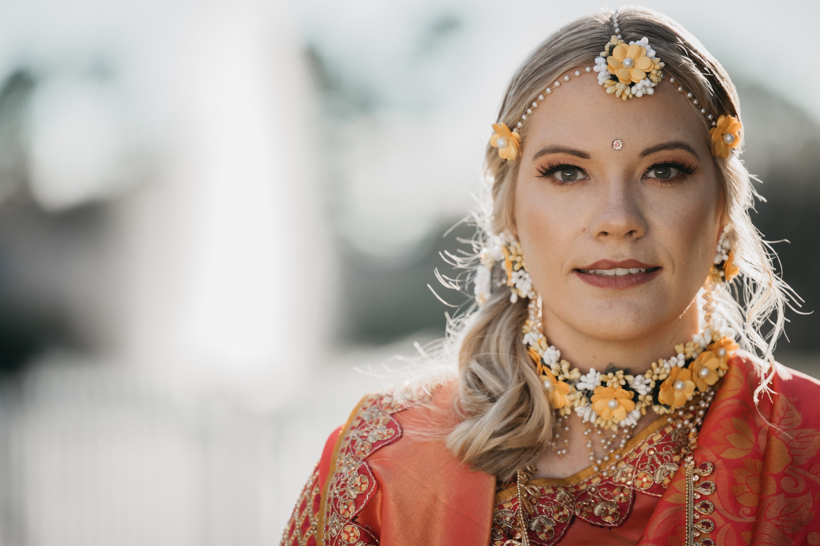 Beautiful bride adorned in yellow and white flowers and a red dress smiles for pictures at her Sanford wedding