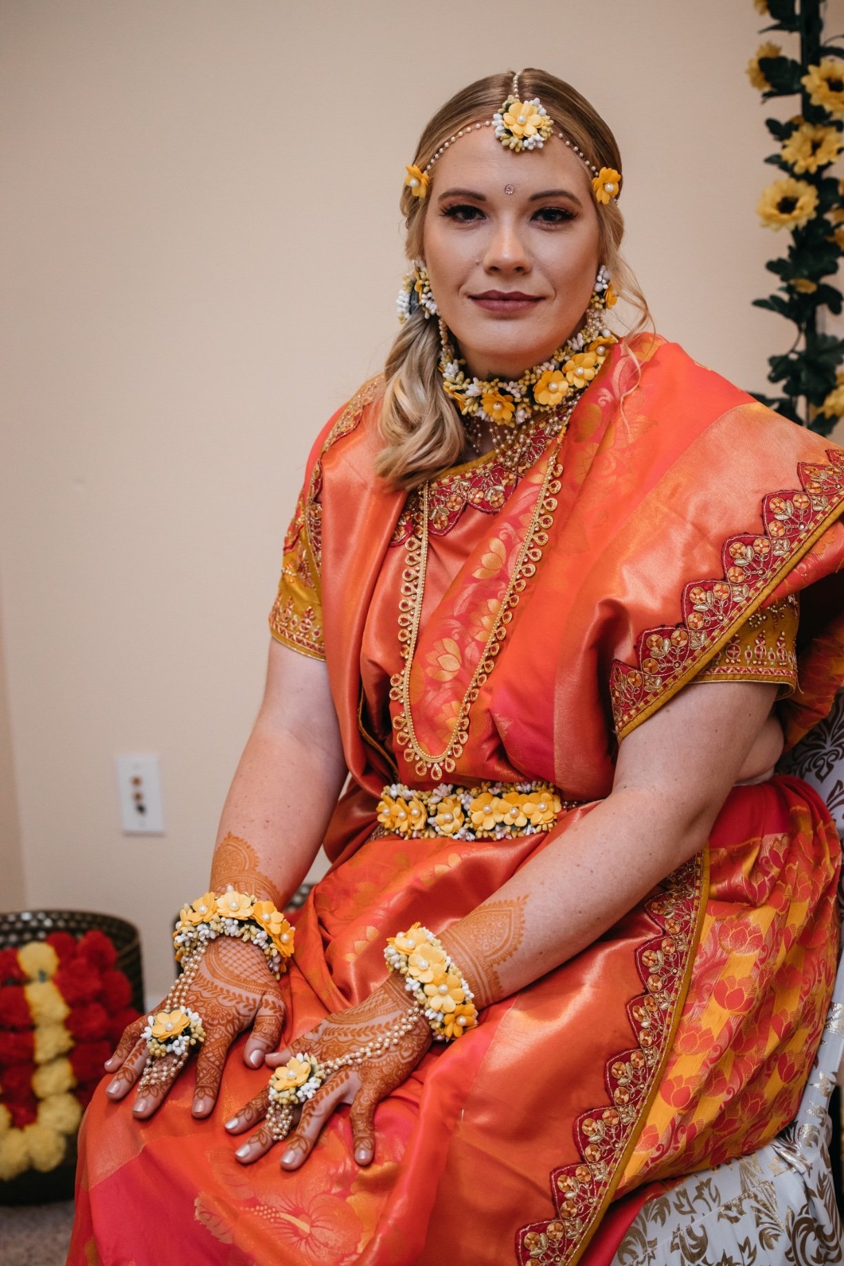 A bride in traditional clothes wears a red dress, henna, and yellow flowers and smiles at her 520 on the water wedding