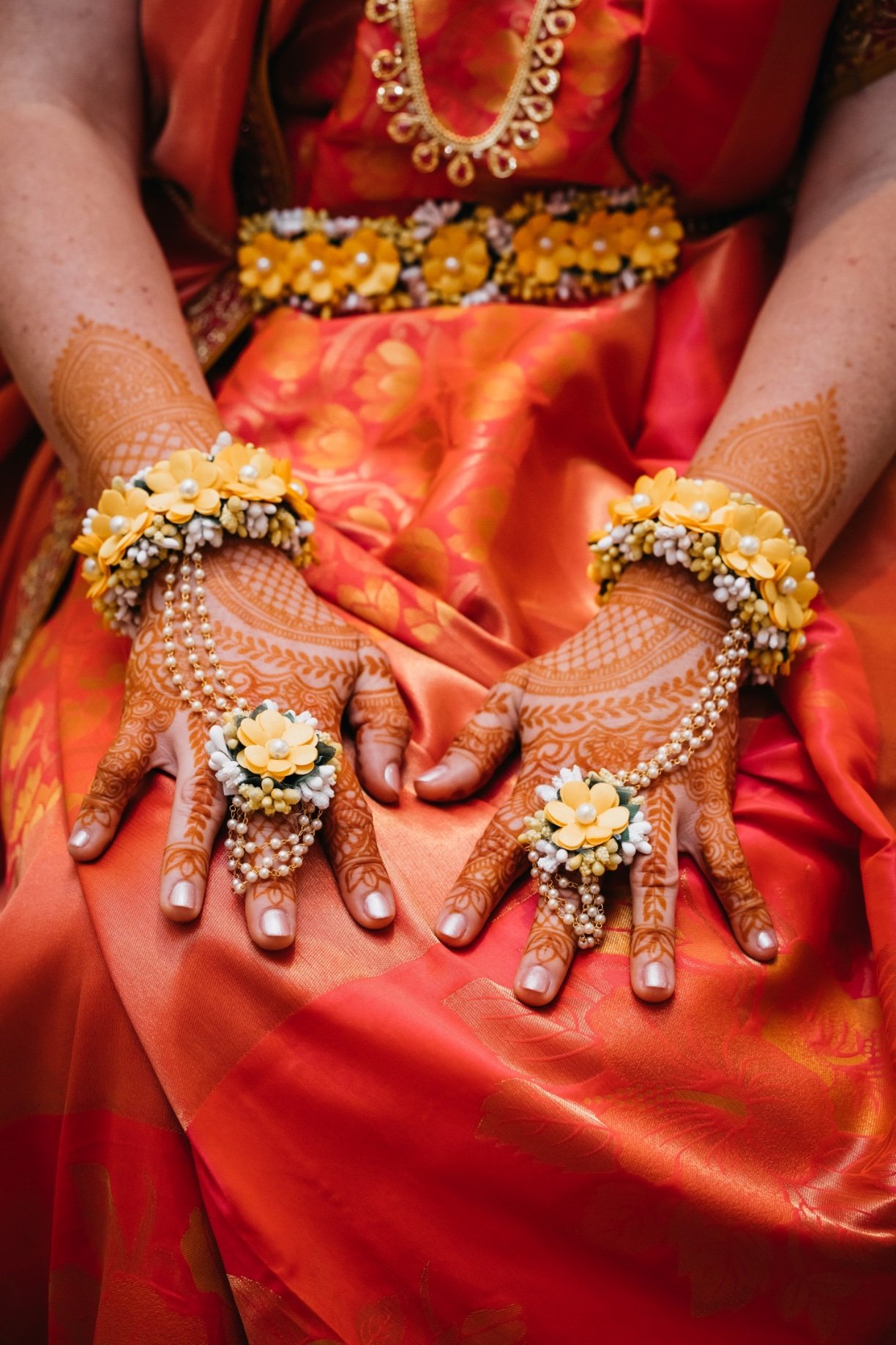 A bride wears henna on her hands with yellow and white flowers and a red dress at her Sanford wedding