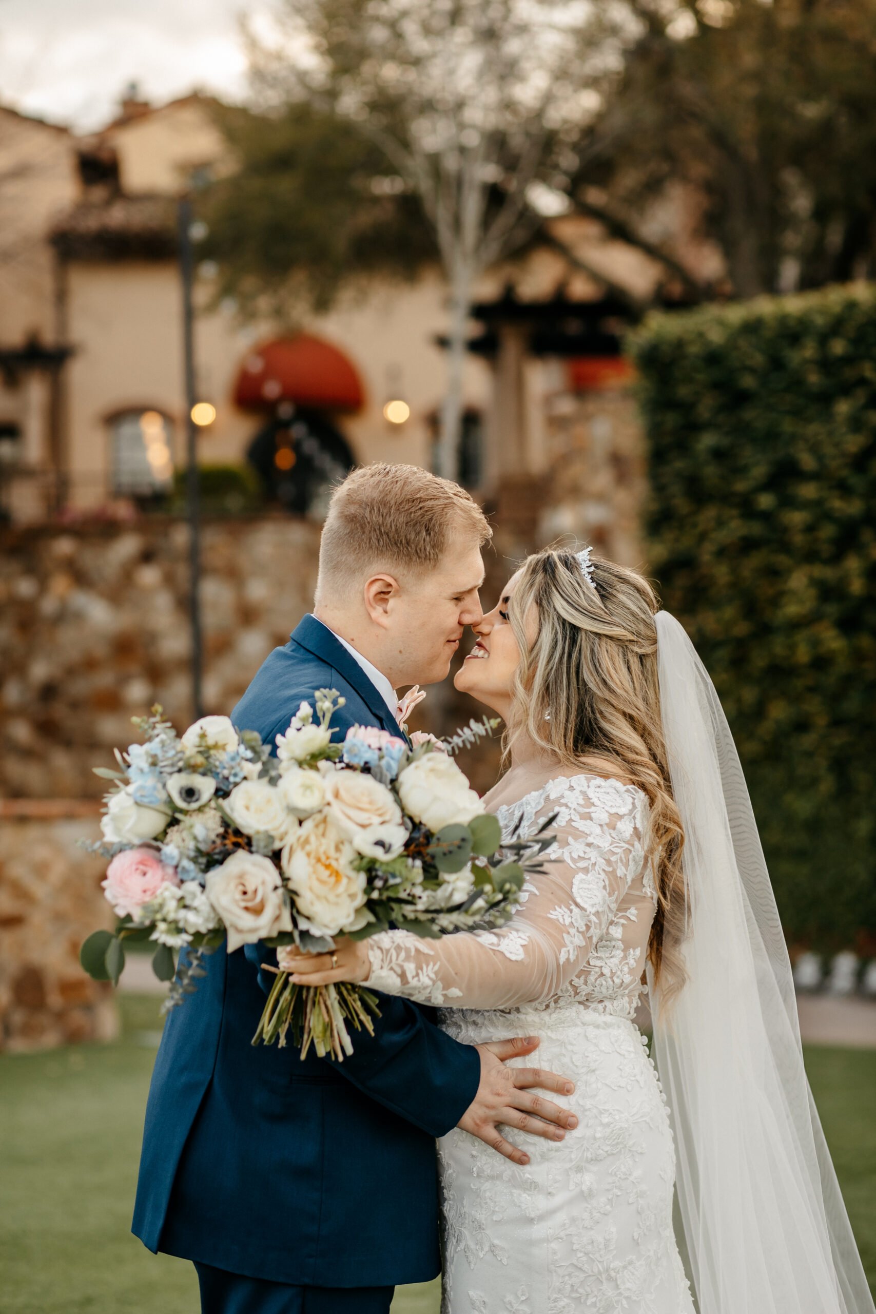 Bride and groom kiss and hold a bouquet of white, blue, and pink flowers at their Bella Collina Orlando FL wedding