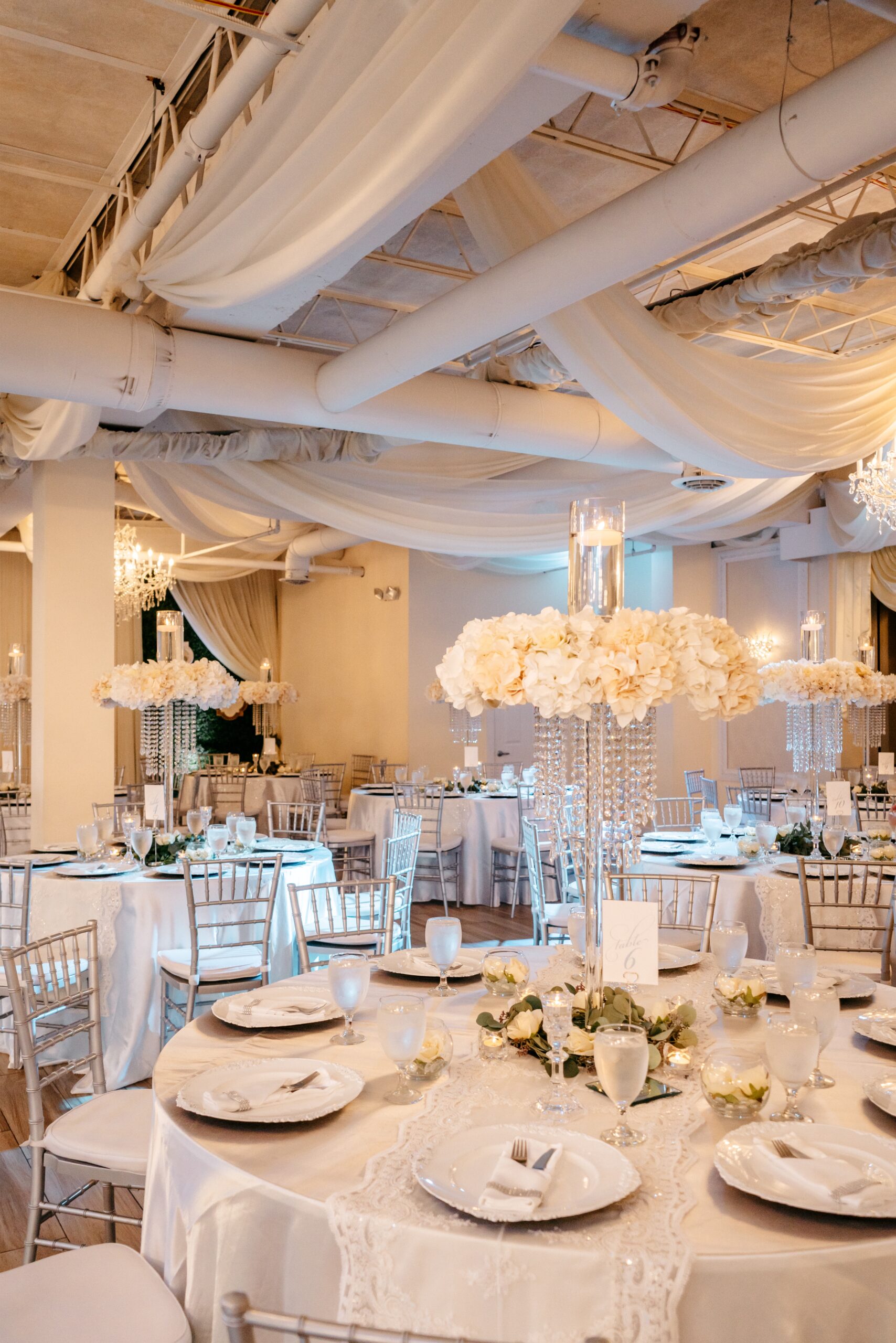 A beautiful ballroom boasts dining tables with white linens, white flowers, and greenery at one of the Central Florida wedding venues