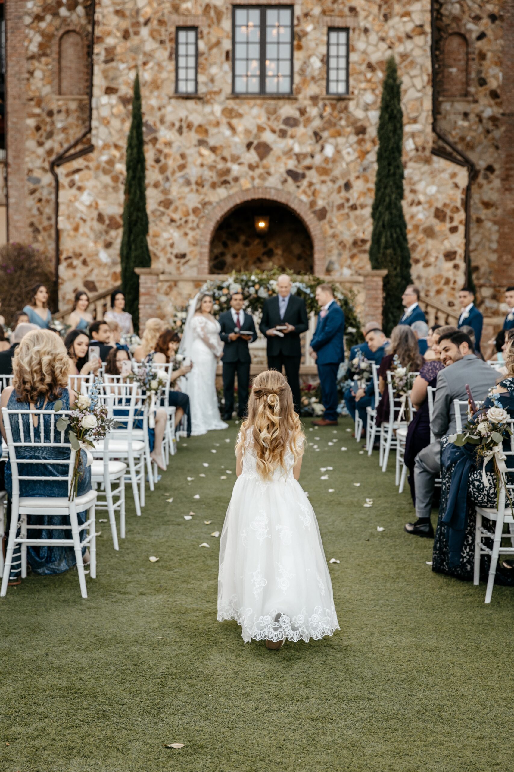 An adorable flower girl in a white dress walks down the aisle to a Bride and Groom at one of the best wedding venues in Central Florida
