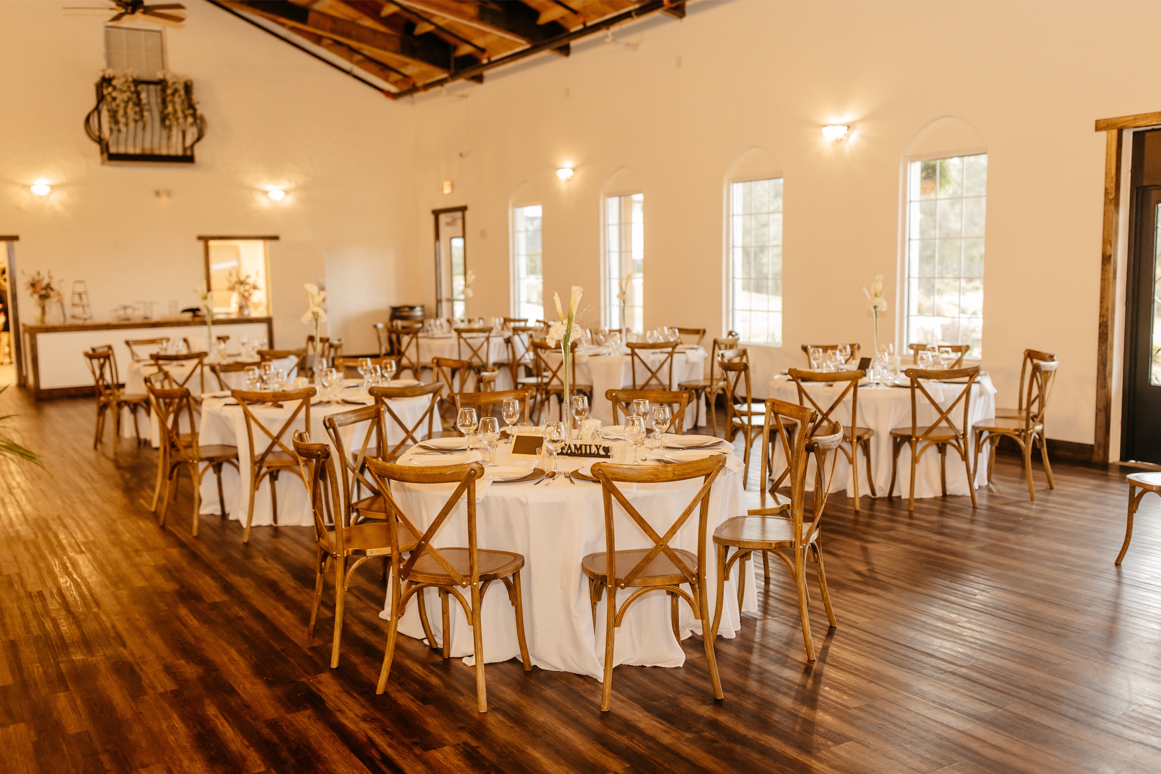 A rustic venue space with wooden floors and chairs is decorated with white linens and beautiful table settings at one of the Central Florida wedding reception venues 