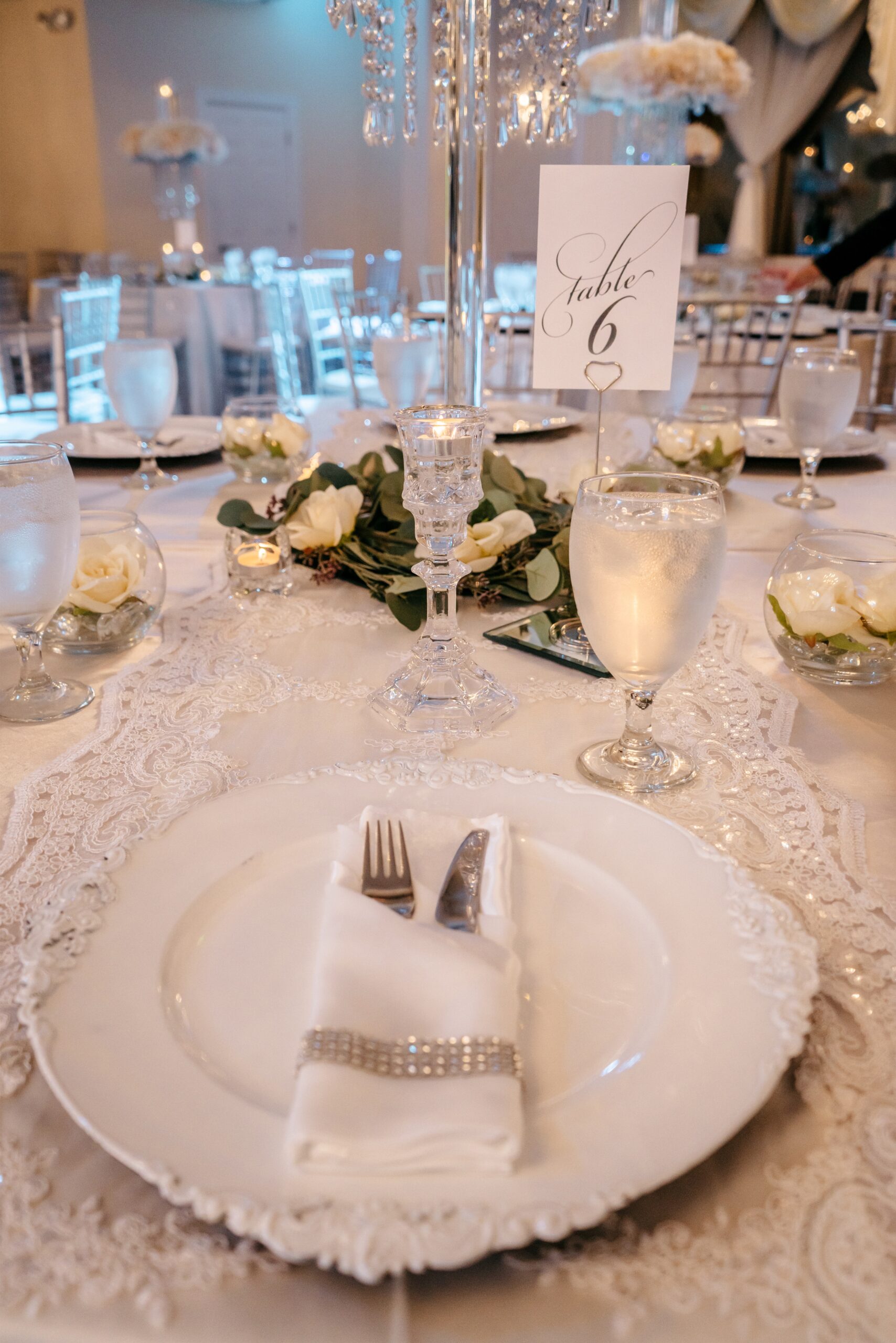 A beautiful dining table at one of the Central Florida wedding reception venues displays crystal galsse and white flowers surrounded by lace and greenery 