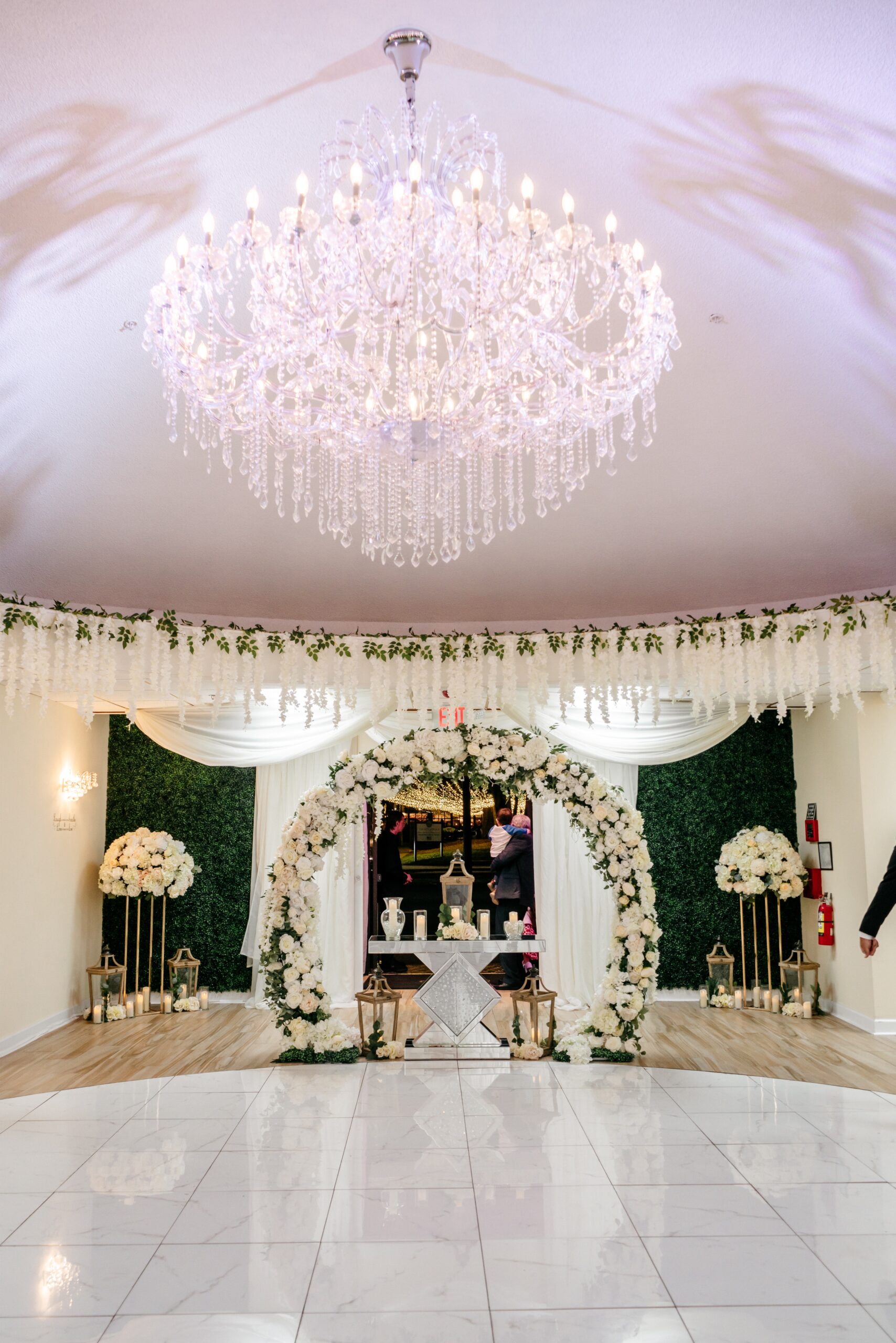 A wedding alter decorated with white flowers and candles surrounded by white and green florals and a beautiful crystal chandelier above it at one of the Central Florida wedding venues