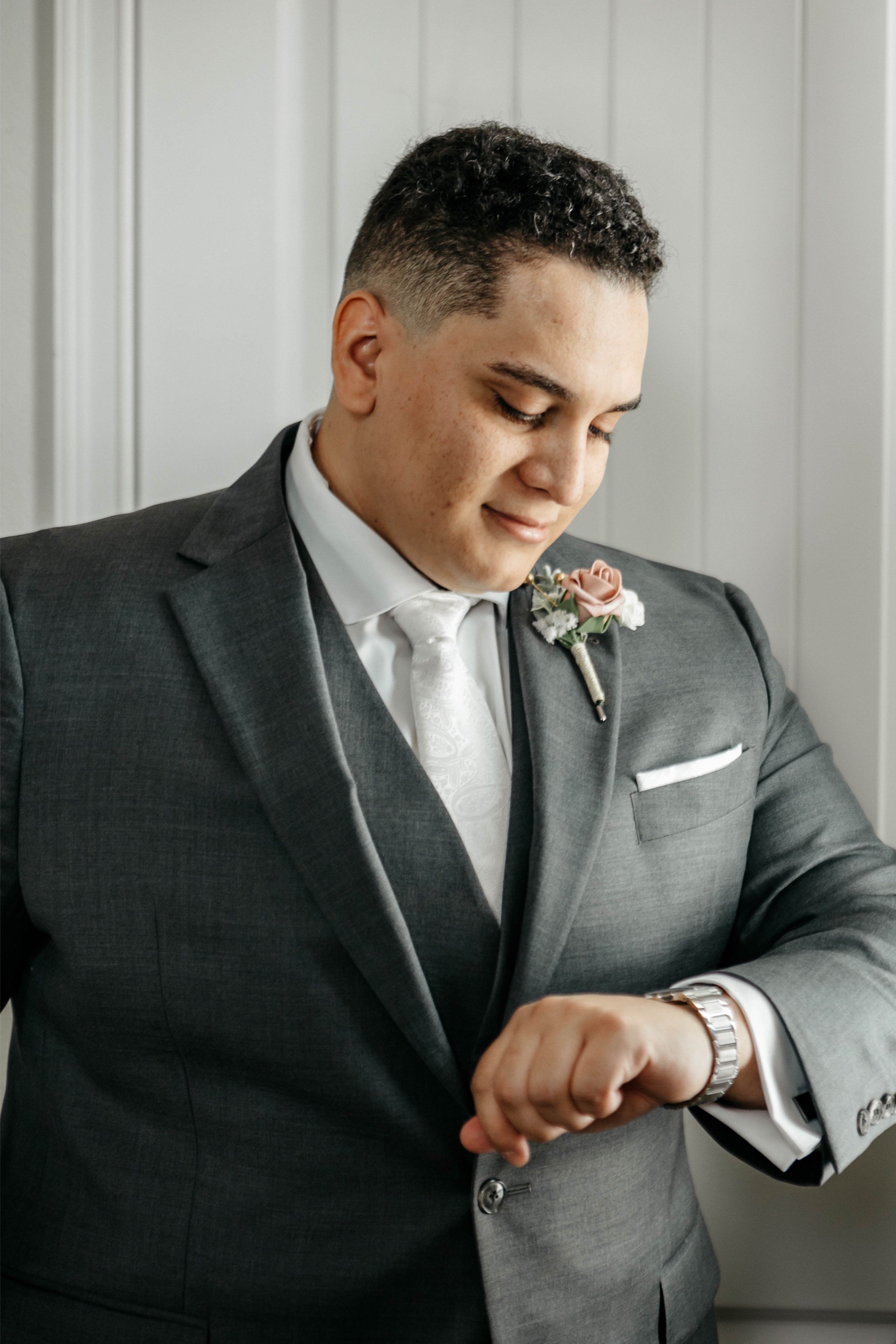 A groom in a dark grey suit looks at his watch while getting ready at his Central Florida wedding venue