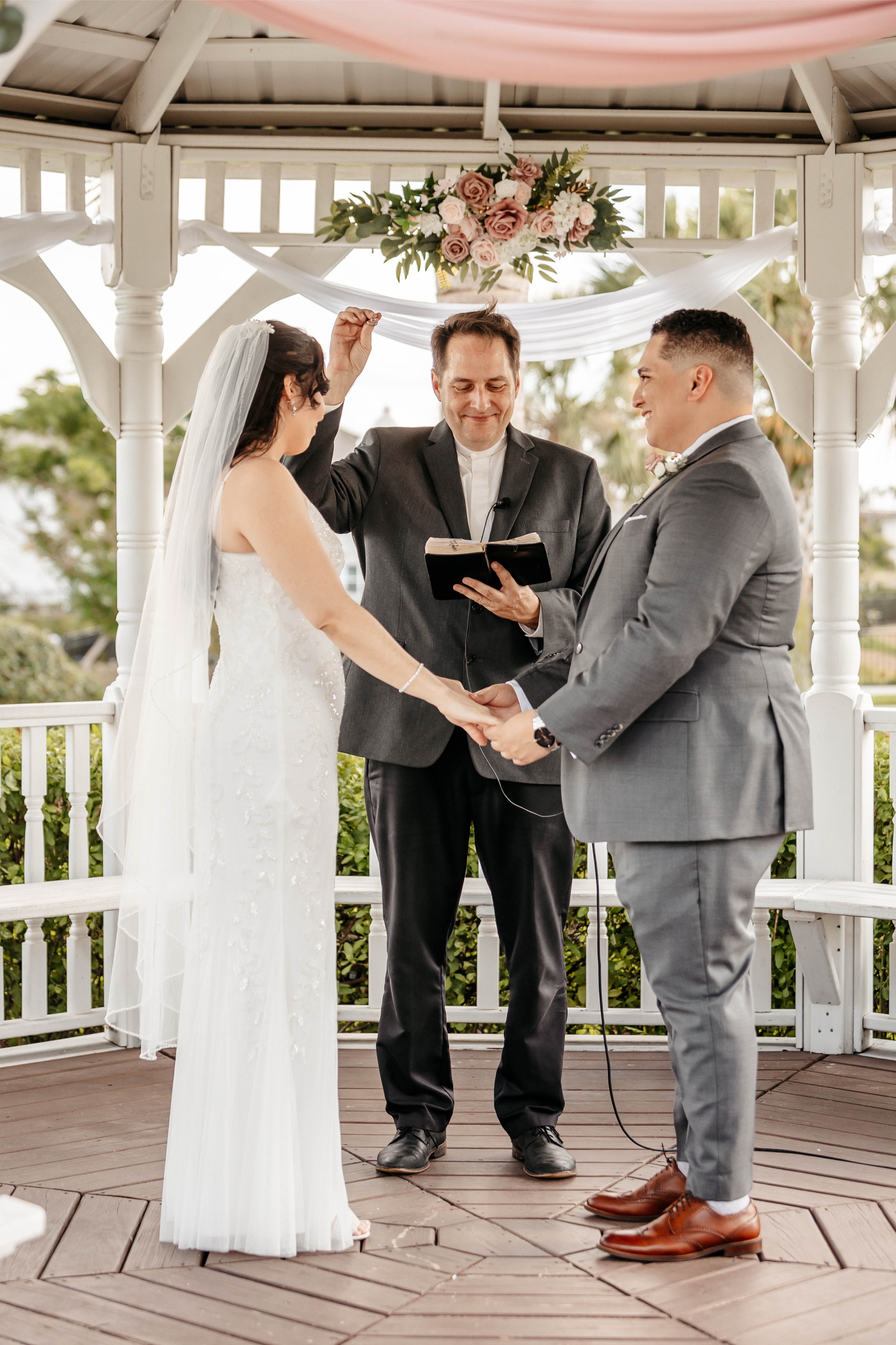 A bride and groom hold hands under a gazebo while the officiant declares them husband and wife at one of the Central Florida wedding venues 