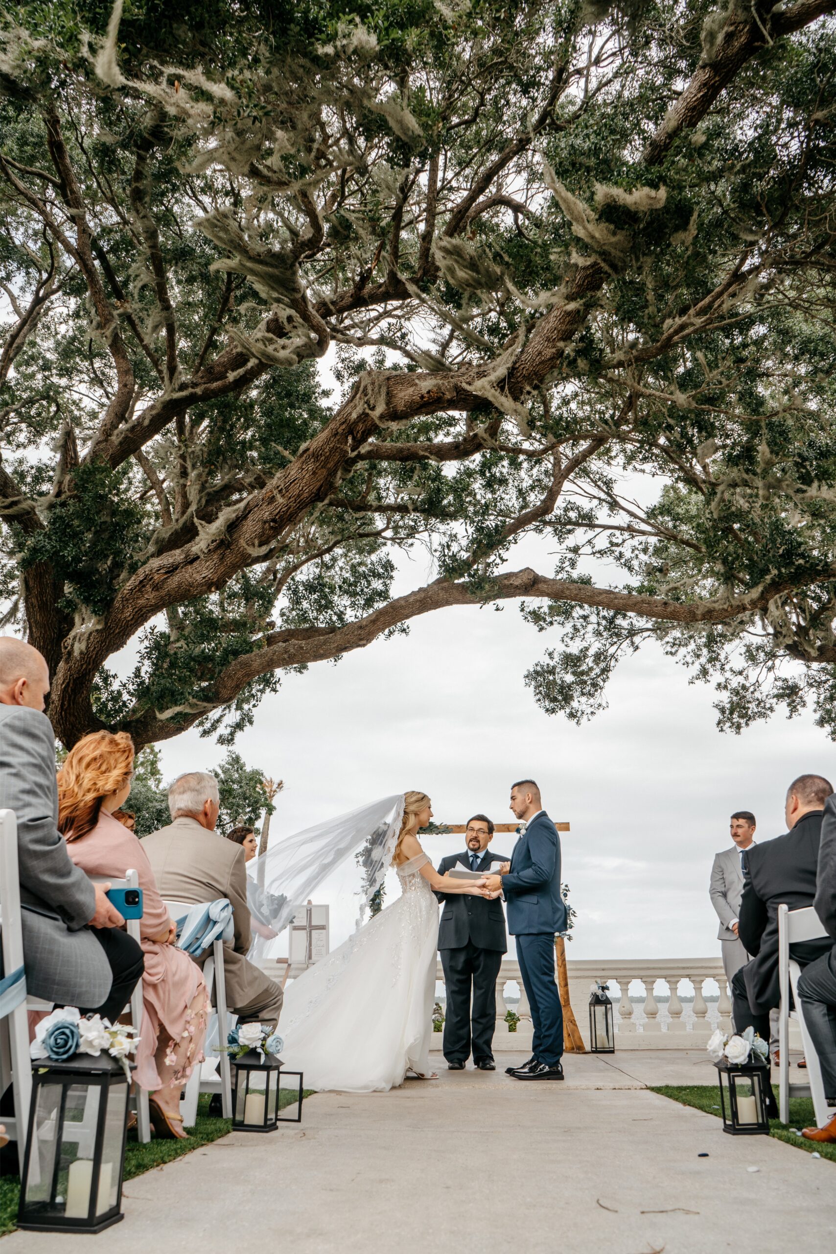 A photo of a bride and groom holding hands at the alter under a beautiful tree by one of the best wedding videographer in Central Florida