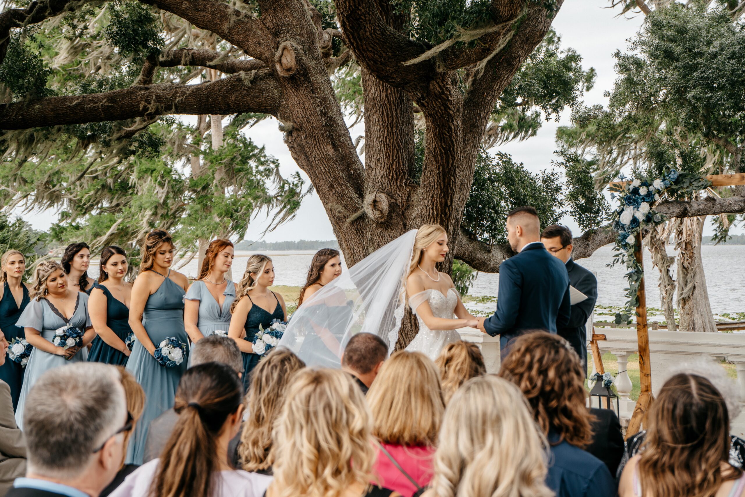Central Florida wedding videographer captures a beautiful moment where a bride's veil flows in the breeze with her bridesmaids in the background at her Florida wedding