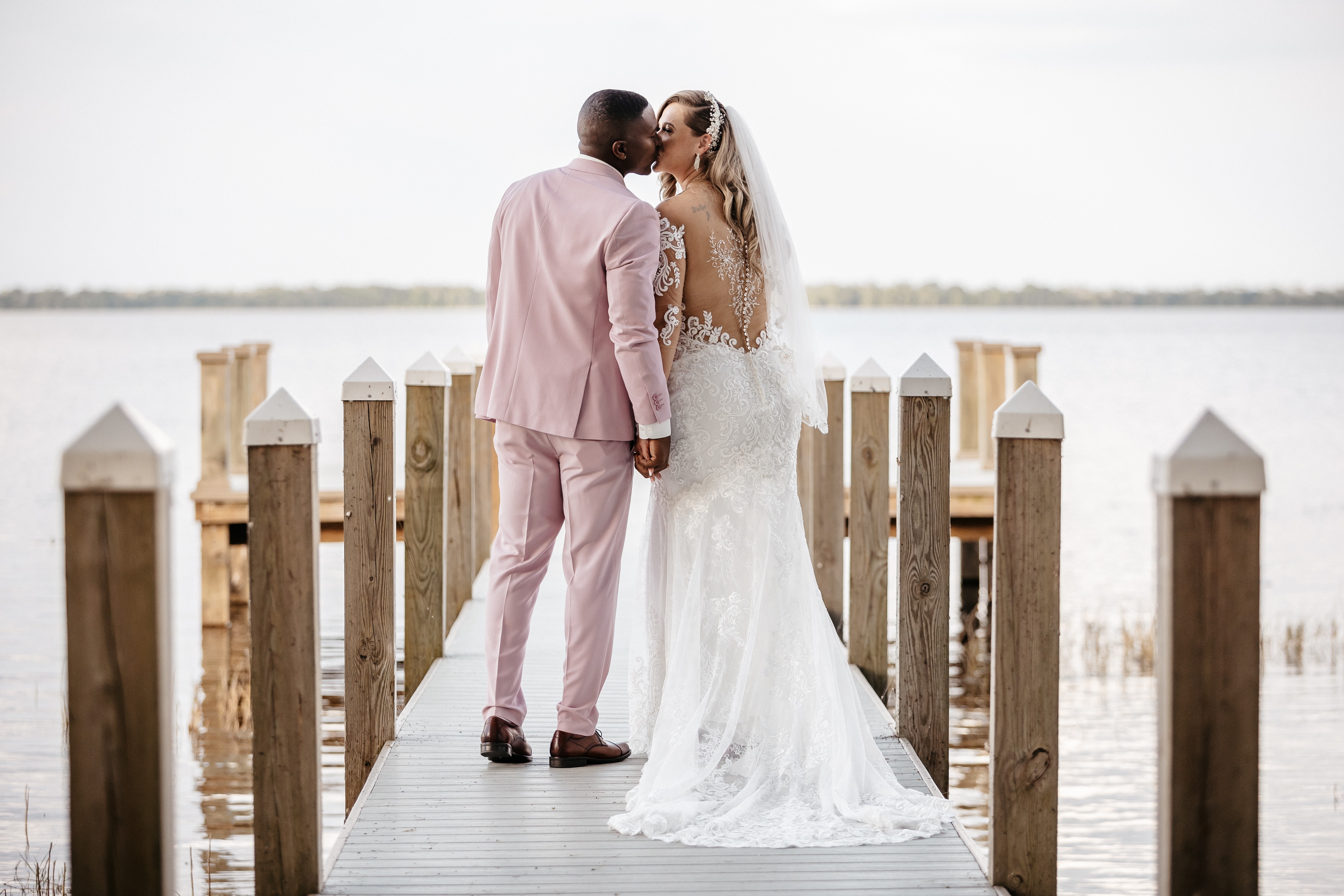 Bride and groom kissing on a wooden dock beside the water during their Florida wedding celebration.