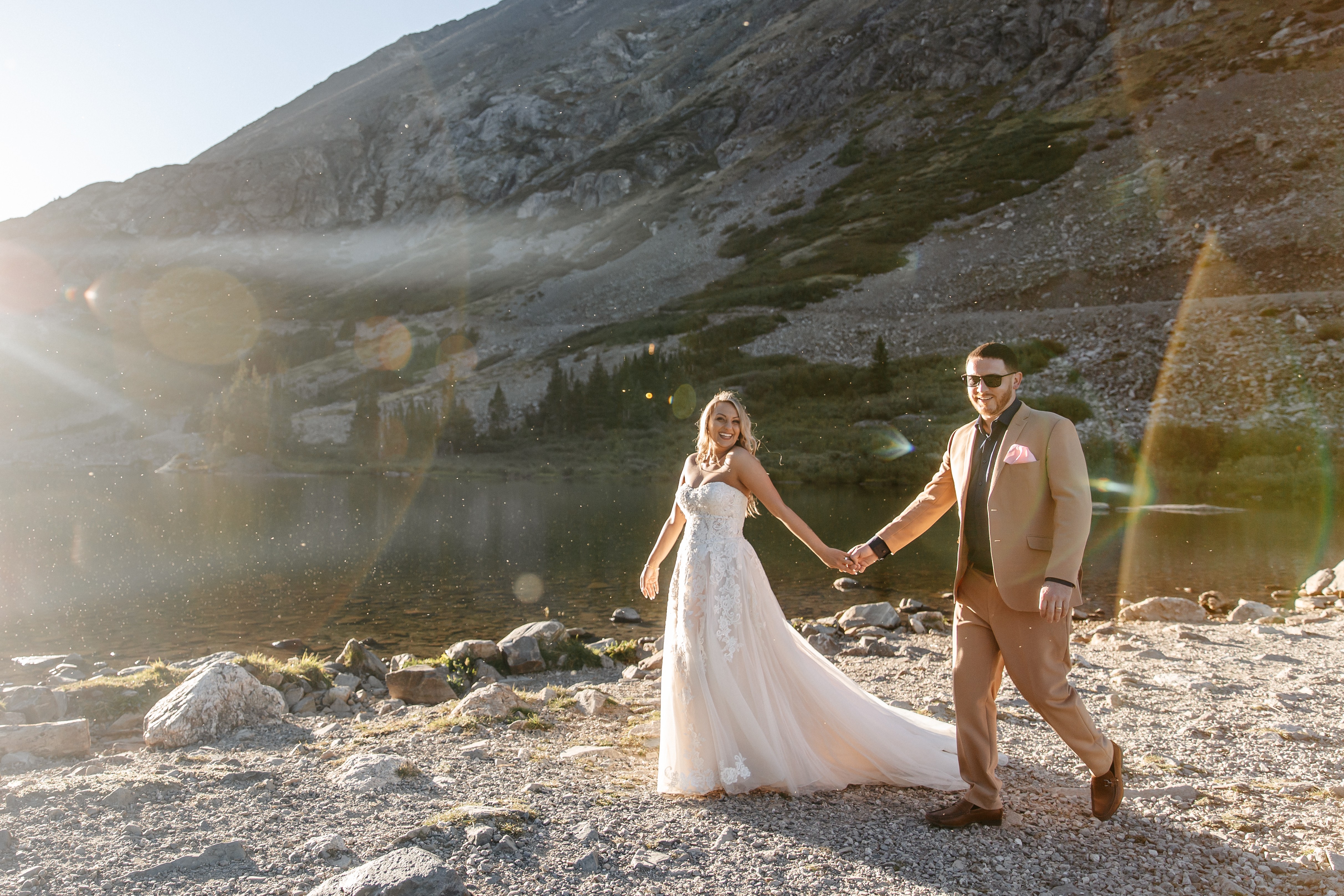 Bride and groom walking hand in hand through a scenic mountain landscape during their wedding portraits.