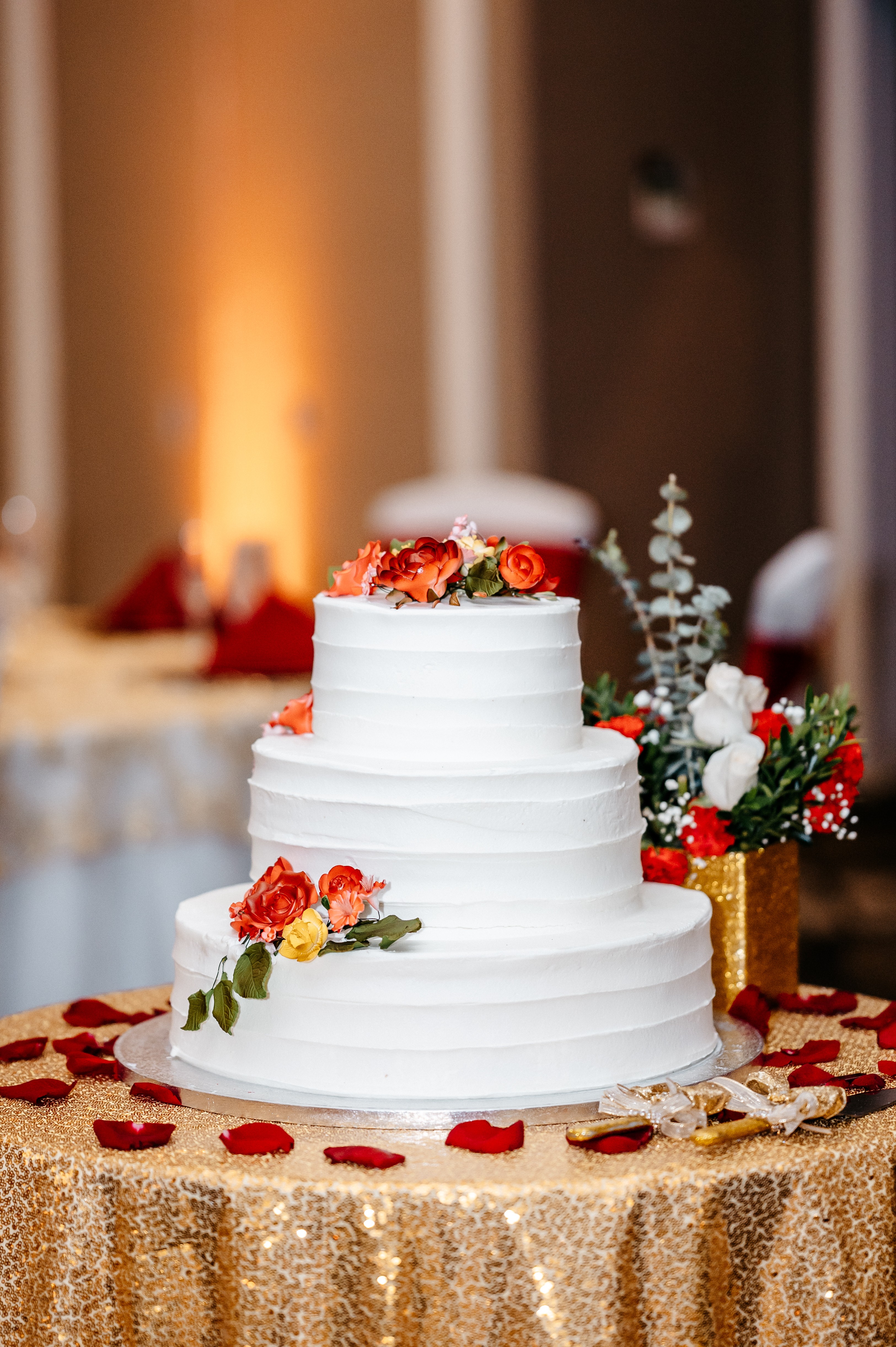 A white wedding cake with red flowers sits on a golden table at the
altamonte springs wedding chapel