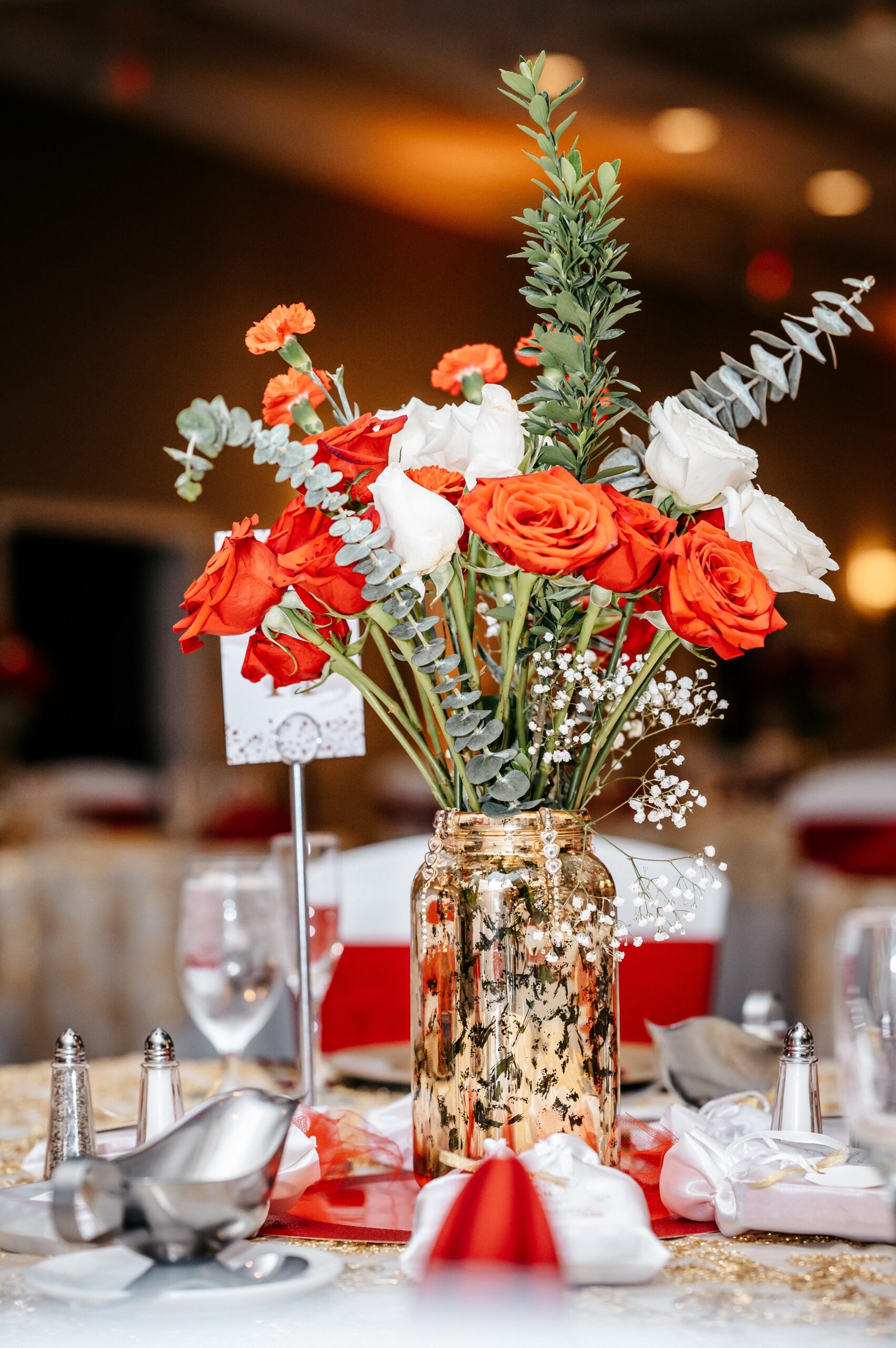 A red and white centerpiece in a golden mason jar decorates a reception table at altamonte chapel