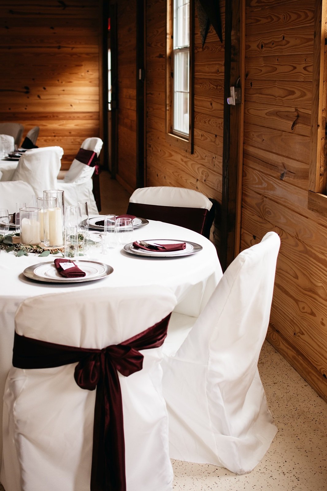 A white reception table with burgundy accent place settings and bows await guests at a 
​wedding venue in bushnell fl