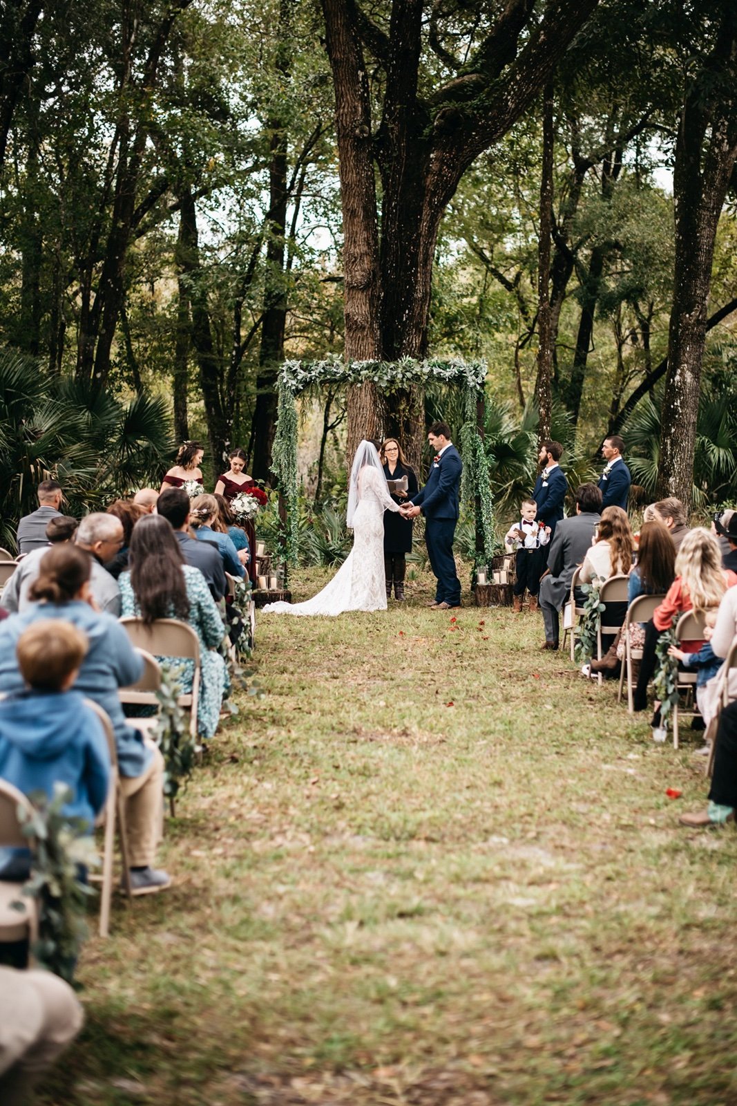 A bride and groom hold hands at the altar and listen to the officiant while standing in front of a forest backdrop at their bushnell wedding