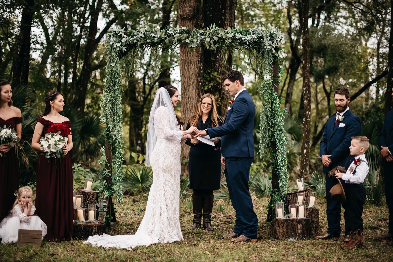 A bride and groom exchange wedding bands at the altar in front of a forest backdrop surrounded by their friends and family at their​wedding venue in bushnell fl