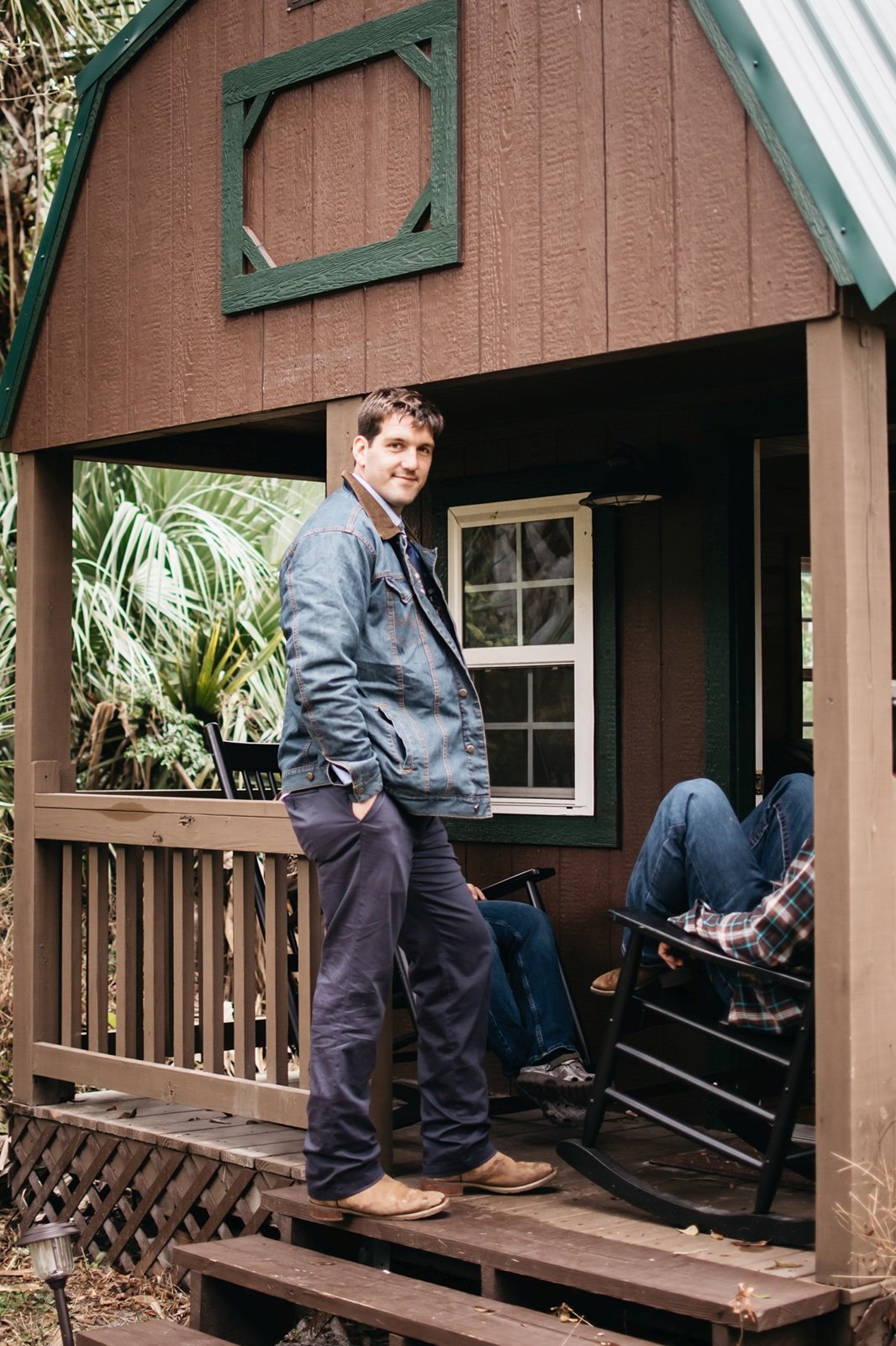 A groomsman in a denim jacket and boots stands on the porch of a small barn with is friends at a
bushnell wedding venue