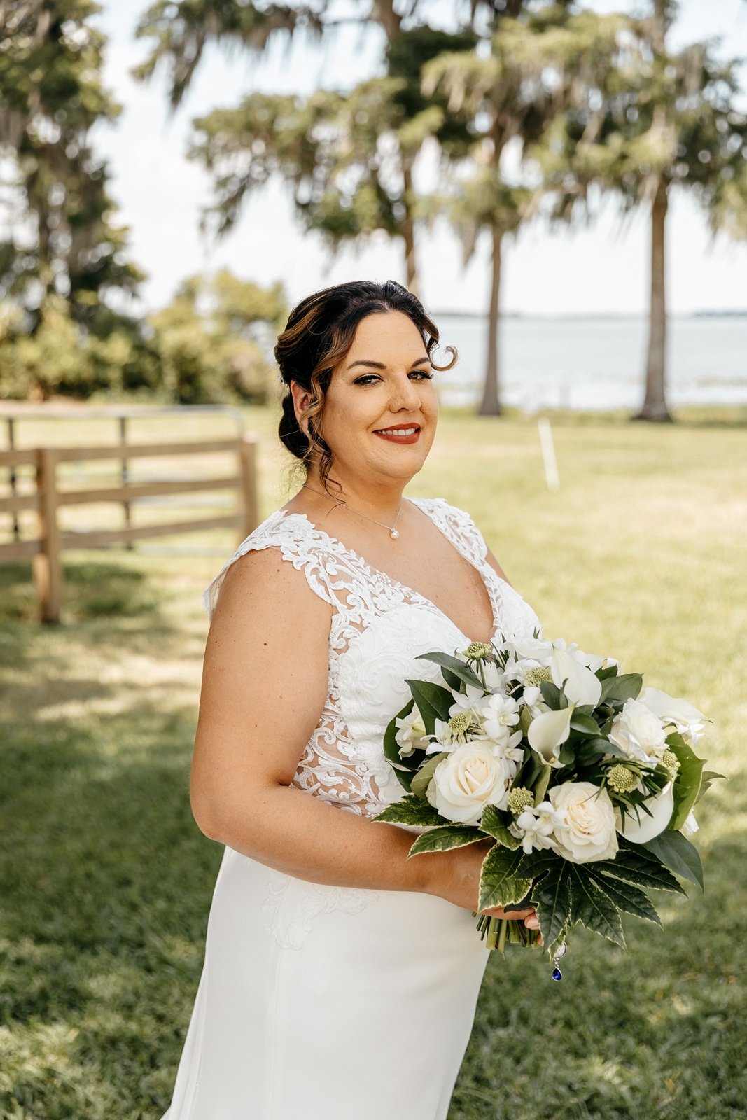 A bride in her wedding dress hold white flowers and stands in front of the ocean at her bella cosa wedding venue