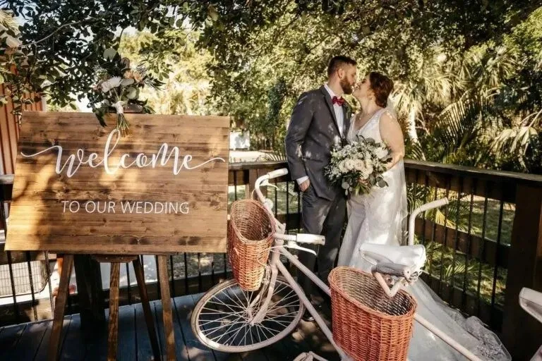 Newlyweds posing beside a welcome sign and vintage bicycle during a Florida wedding celebration.