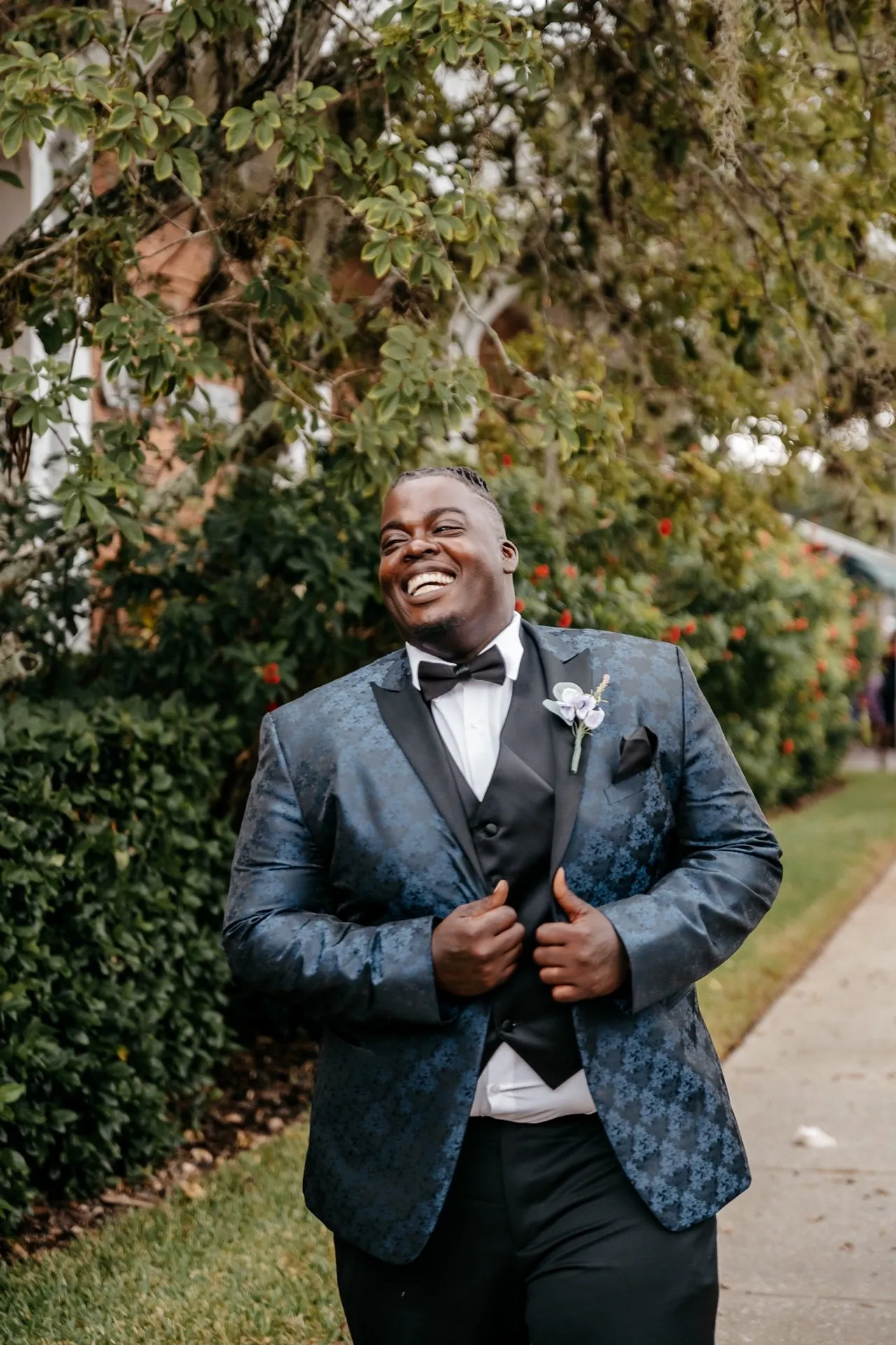 A groom wearing a blue pattern tuxedo smiles as he gets ready for his wedding