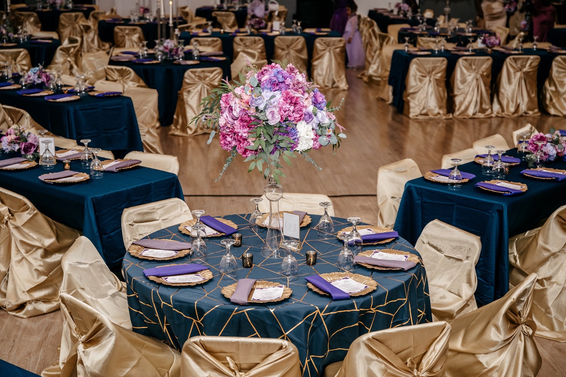 A wedding reception decorated in gold and blue with pink and purple flowers