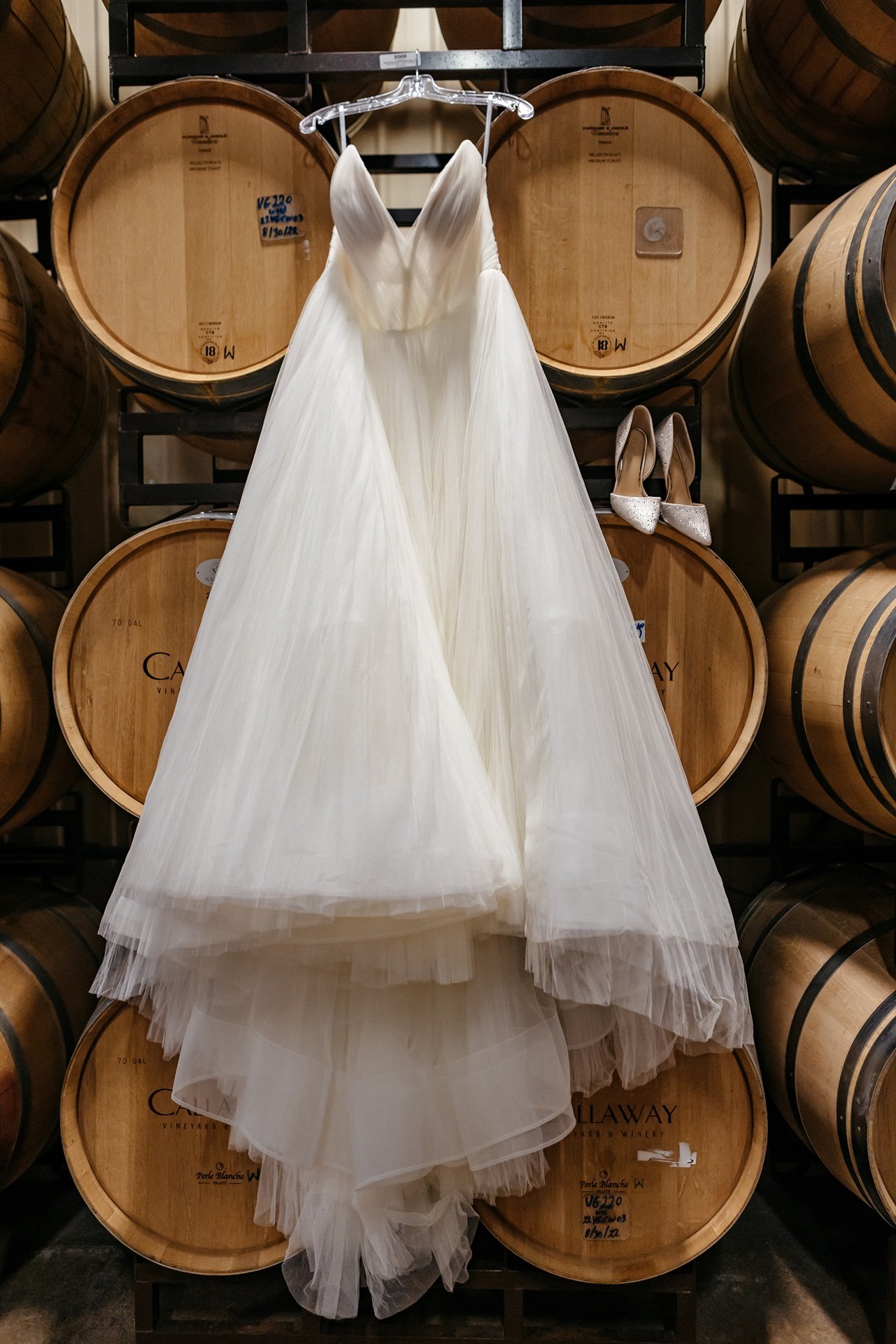 A wedding dress is displayed in front of a wall of barrels at a wedding venue in Central Florida